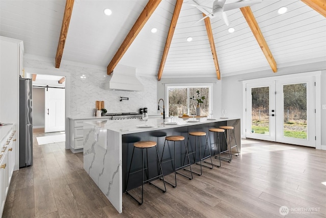 kitchen featuring a barn door, a ceiling fan, wood finished floors, vaulted ceiling with beams, and backsplash