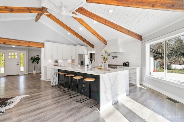 kitchen with a kitchen bar, tasteful backsplash, custom range hood, and stainless steel refrigerator with ice dispenser