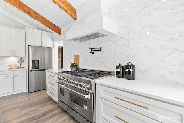 kitchen with vaulted ceiling with beams, premium range hood, white cabinets, appliances with stainless steel finishes, and backsplash