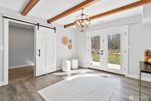 doorway to outside with a barn door, beam ceiling, visible vents, and wood finished floors