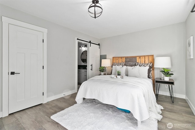 bedroom featuring a barn door, baseboards, light wood-style flooring, and ensuite bathroom