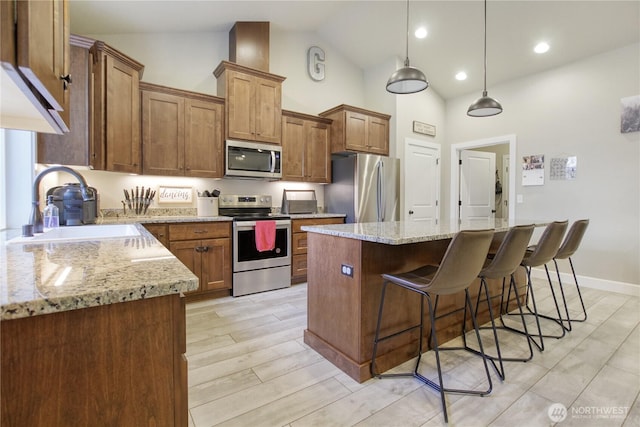 kitchen with a center island, pendant lighting, appliances with stainless steel finishes, brown cabinetry, and a sink