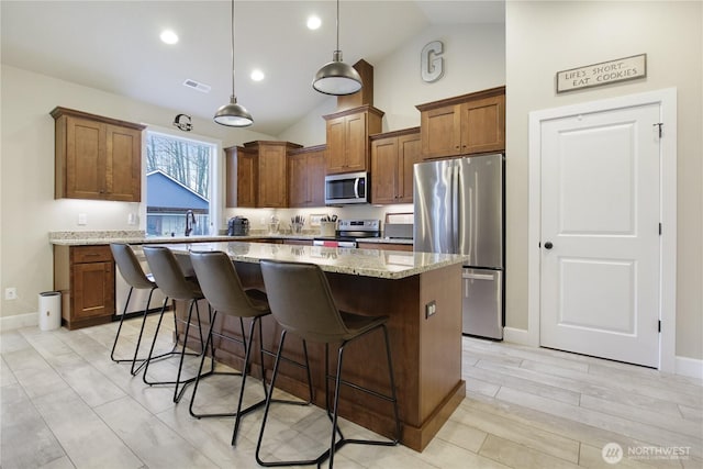 kitchen with light stone counters, a center island, pendant lighting, brown cabinets, and stainless steel appliances