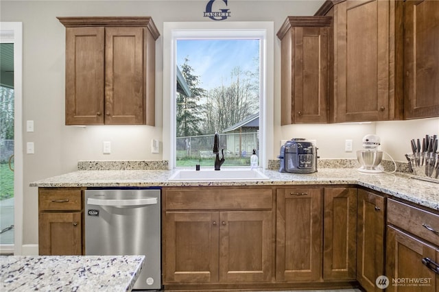 kitchen with brown cabinetry, dishwasher, light stone counters, and a sink