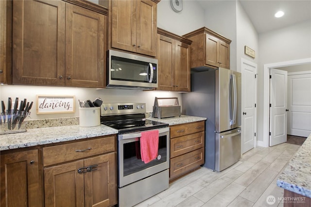 kitchen with stainless steel appliances, light stone counters, light wood-type flooring, and brown cabinets