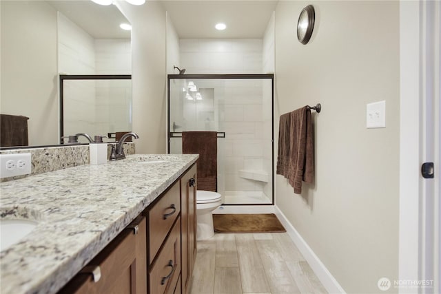 full bathroom featuring toilet, wood finished floors, vanity, baseboards, and a stall shower