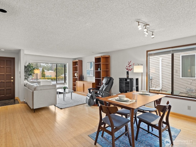 dining space featuring a textured ceiling, light wood-style flooring, and baseboards