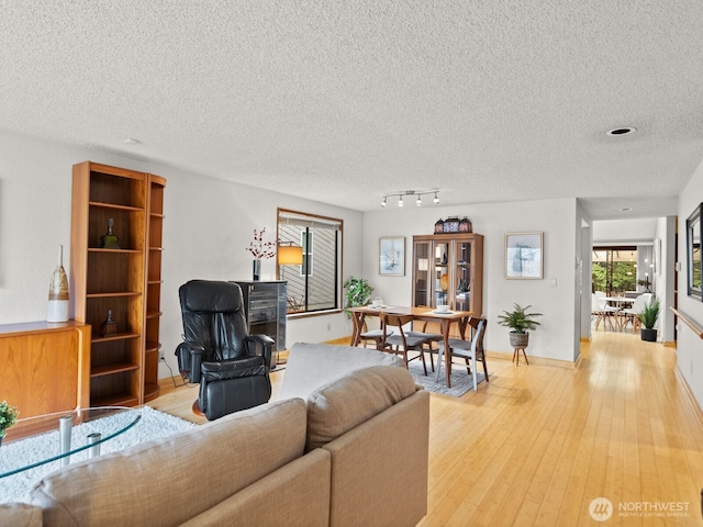 living area with a textured ceiling, light wood-type flooring, and baseboards