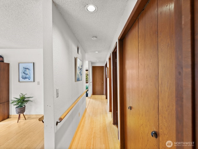 hall featuring light wood-style floors, a textured wall, and a textured ceiling