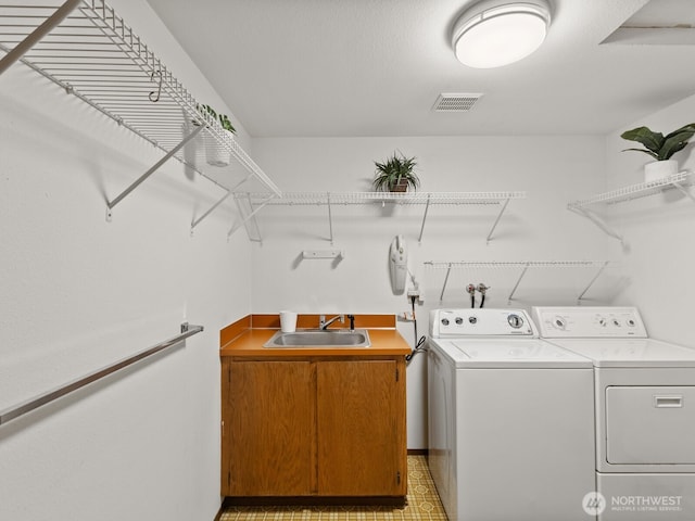 washroom featuring cabinet space, a sink, visible vents, and washing machine and clothes dryer