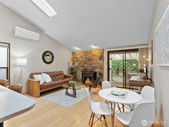 living room with lofted ceiling with skylight, wood finished floors, a textured ceiling, a stone fireplace, and a wall mounted AC