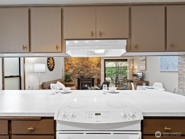 kitchen with white electric stove, ventilation hood, light countertops, and a stone fireplace