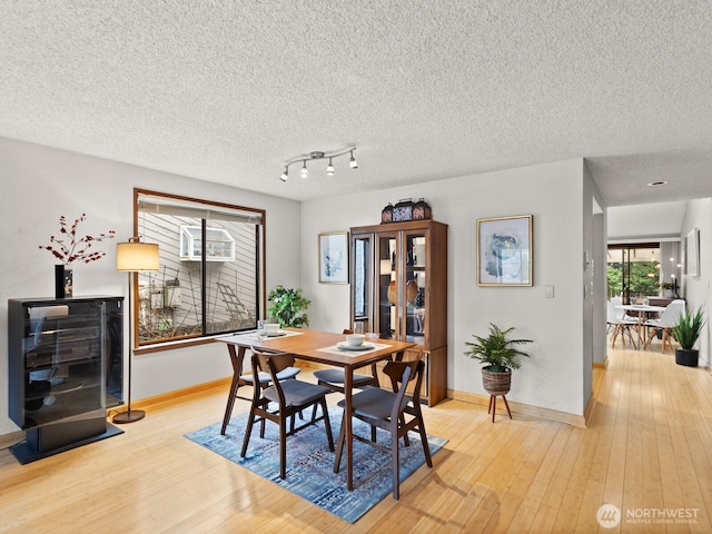 dining room with light wood-type flooring, a textured ceiling, and baseboards