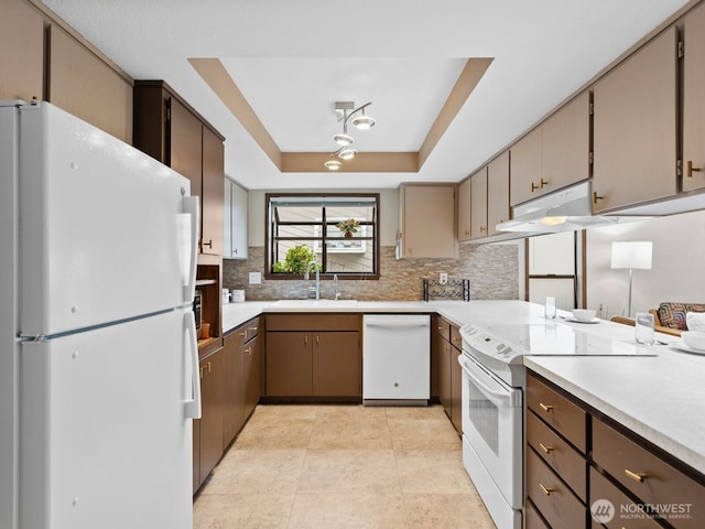 kitchen featuring white appliances, decorative backsplash, a raised ceiling, light countertops, and a sink