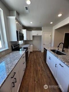 kitchen with light stone counters, dark wood-style flooring, stainless steel appliances, white cabinets, and a sink