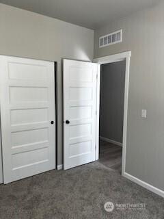 unfurnished bedroom with a closet, visible vents, dark carpet, and baseboards