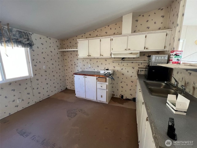 kitchen featuring lofted ceiling, wallpapered walls, white cabinets, and a sink