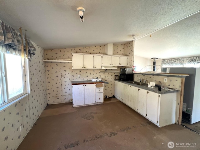 kitchen with dark countertops, vaulted ceiling, a sink, and wallpapered walls