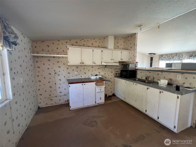 kitchen featuring dark countertops, a sink, under cabinet range hood, and wallpapered walls