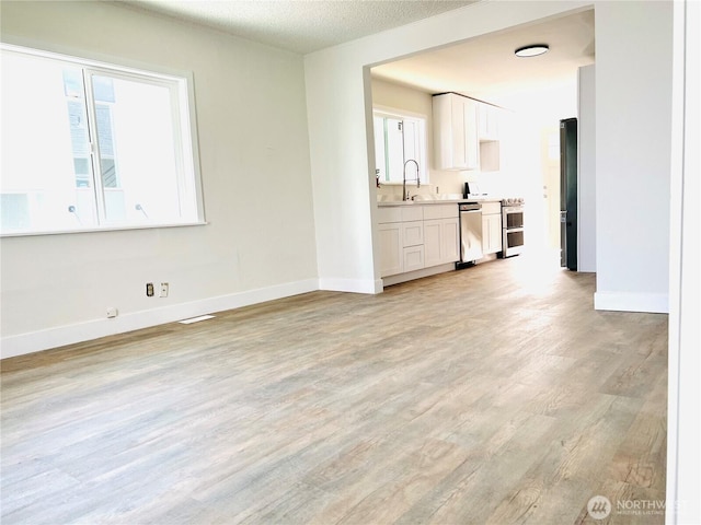 unfurnished living room with light wood finished floors, a textured ceiling, baseboards, and a sink