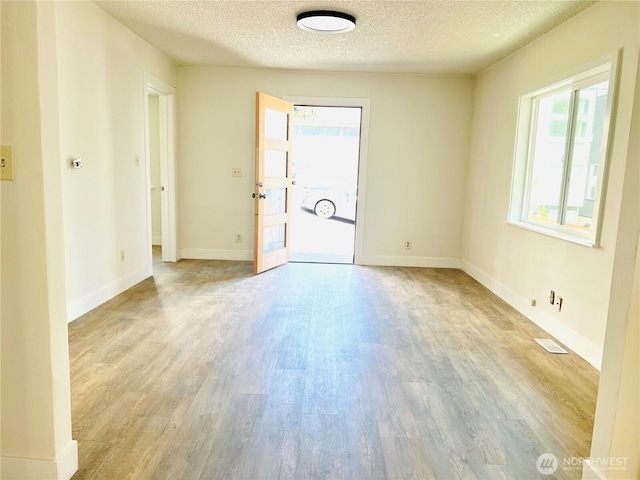 spare room with visible vents, a textured ceiling, baseboards, and wood finished floors