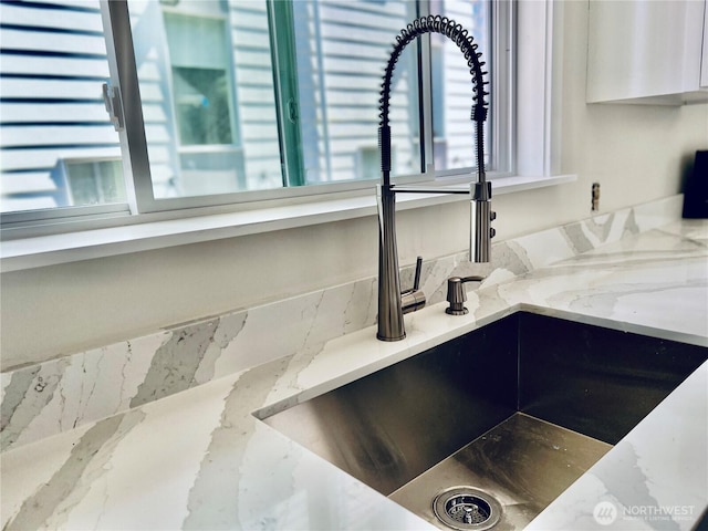 details featuring light stone counters, white cabinets, and a sink