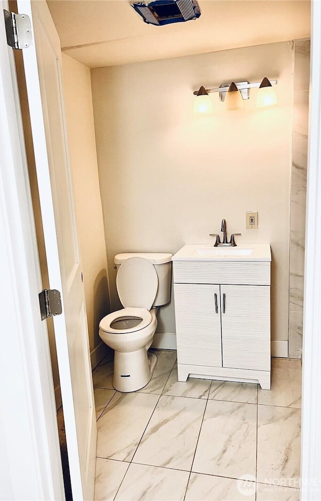 half bath featuring toilet, marble finish floor, baseboards, and vanity