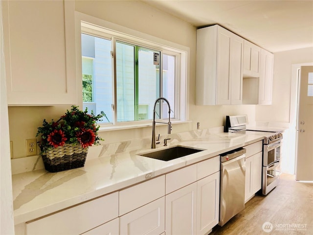 kitchen with appliances with stainless steel finishes, white cabinets, a sink, light stone countertops, and light wood-type flooring