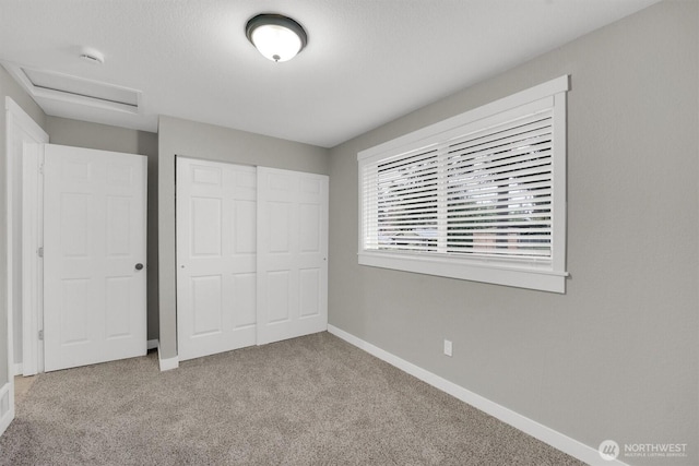 unfurnished bedroom featuring a closet, baseboards, carpet, and attic access