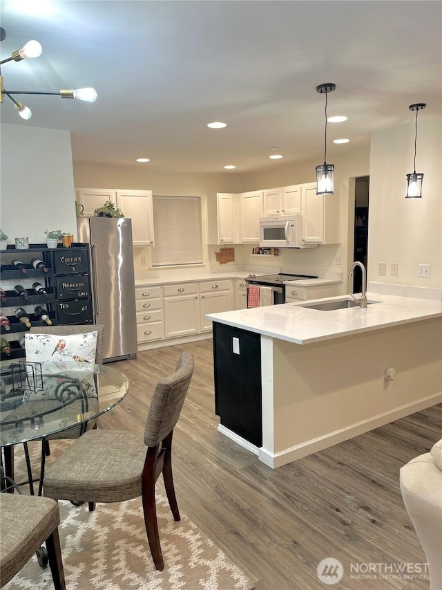 kitchen with white cabinets, a peninsula, stainless steel appliances, light wood-type flooring, and a sink