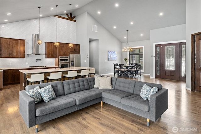 living room featuring baseboards, high vaulted ceiling, wood finished floors, and an inviting chandelier