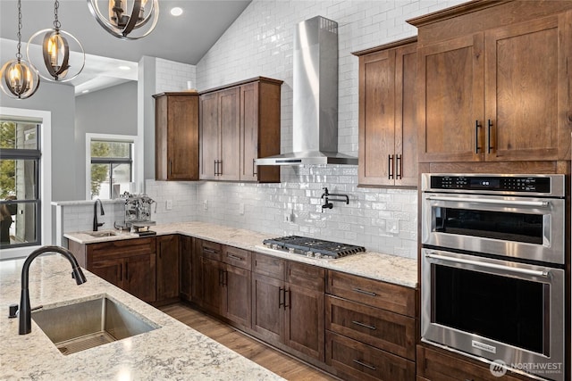 kitchen featuring appliances with stainless steel finishes, vaulted ceiling, a sink, and wall chimney range hood