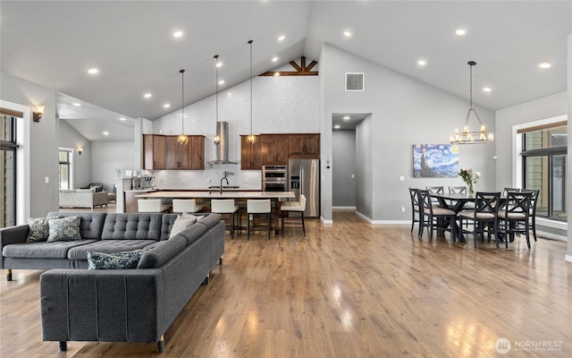 living room featuring high vaulted ceiling, light wood finished floors, visible vents, and a healthy amount of sunlight