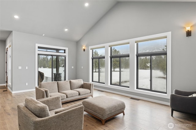 living area with high vaulted ceiling, light wood-type flooring, visible vents, and baseboards