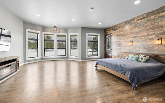 bedroom featuring baseboards, a glass covered fireplace, an accent wall, wood finished floors, and recessed lighting