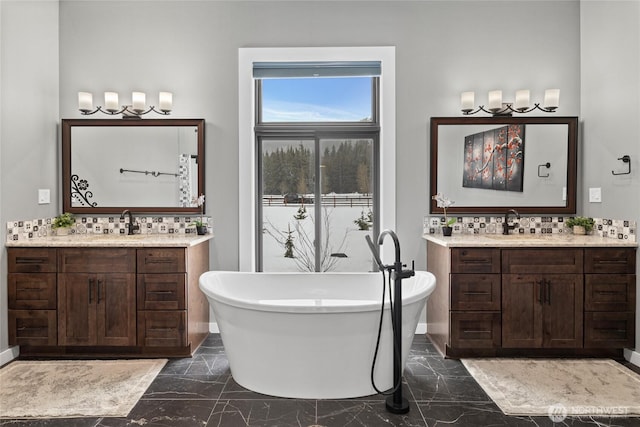 full bath featuring marble finish floor, two vanities, a freestanding bath, and a sink