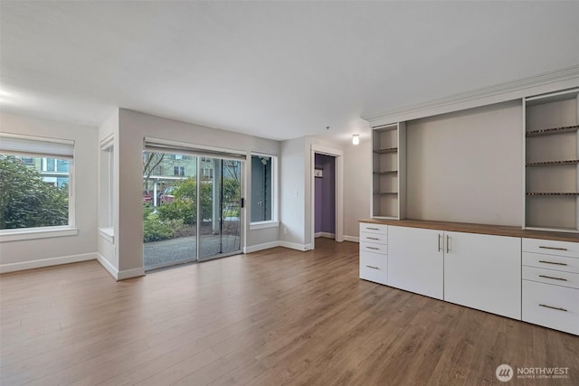 unfurnished living room with light wood-type flooring, a wealth of natural light, and baseboards