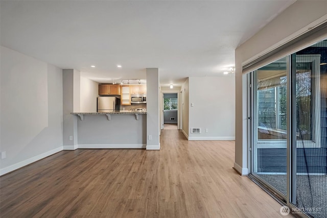 unfurnished living room featuring baseboards, light wood finished floors, visible vents, and a healthy amount of sunlight