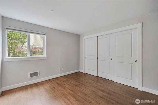 unfurnished bedroom featuring a closet, wood finished floors, visible vents, and baseboards