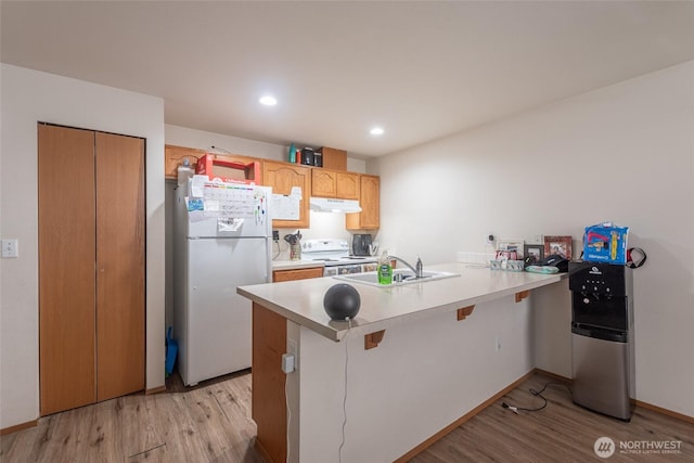 kitchen with a peninsula, white appliances, light countertops, and under cabinet range hood