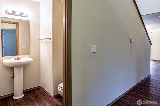 interior space featuring toilet, a sink, baseboards, and wood finished floors