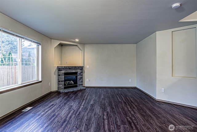 unfurnished living room featuring a glass covered fireplace, dark wood finished floors, visible vents, and baseboards