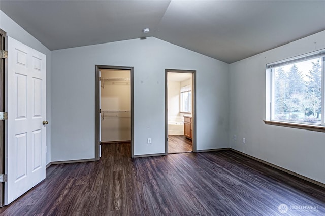 unfurnished bedroom featuring baseboards, vaulted ceiling, a closet, dark wood-style floors, and a walk in closet