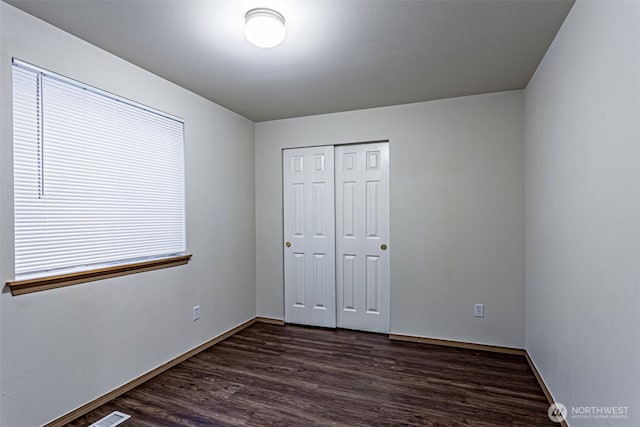 unfurnished bedroom with a closet, baseboards, and dark wood-style flooring