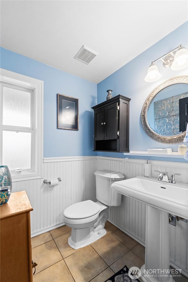 bathroom featuring tile patterned flooring, wainscoting, visible vents, and toilet