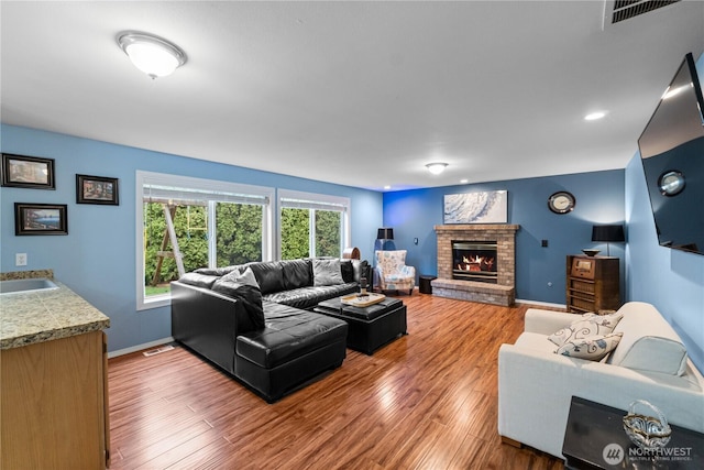 living area with a brick fireplace, visible vents, baseboards, and wood finished floors