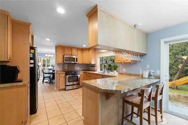 kitchen featuring light tile patterned floors, a breakfast bar area, appliances with stainless steel finishes, a peninsula, and a sink