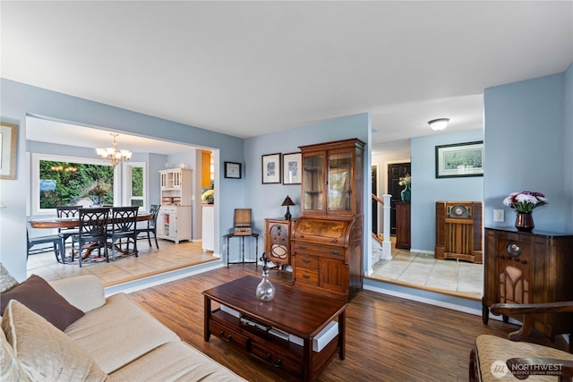 living room featuring stairs, an inviting chandelier, baseboards, and light wood-style floors