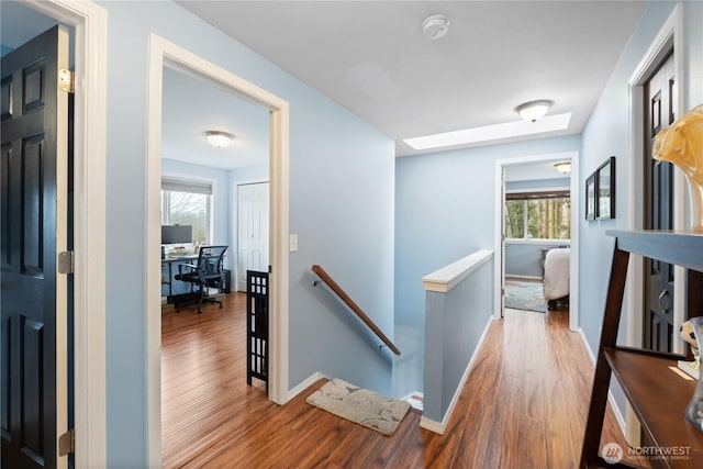 corridor with wood finished floors, an upstairs landing, and baseboards