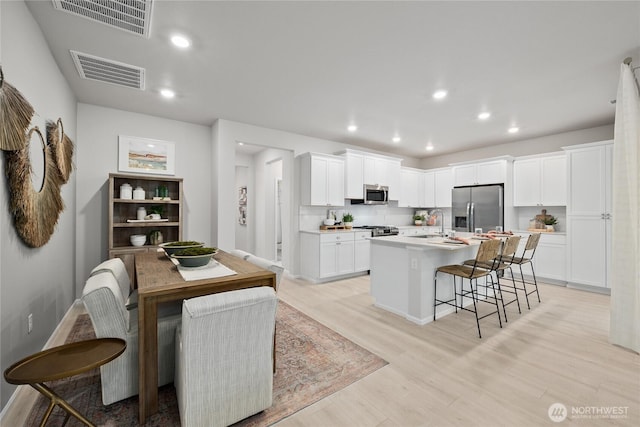 kitchen with light countertops, visible vents, appliances with stainless steel finishes, white cabinetry, and an island with sink